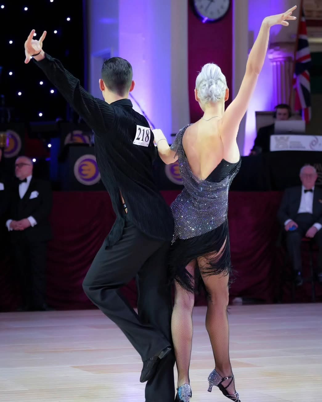 Tatiana Vaccaro in a silver Latin dress extending her arm in an elegant line with her partner on a ballroom floor