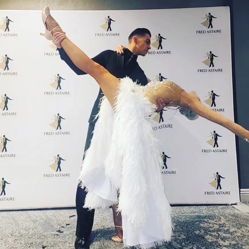 Tatiana Vaccaro in a white feathered gown in a dramatic layback with her partner at a Fred Astaire event